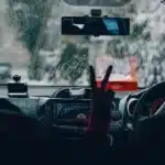 Motorista dirigindo sob forte chuva, com o para-brisa coberto por gotas e baixa visibilidade à frente, simbolizando a importância da manutenção preventiva para evitar aquaplanagem e falhas elétricas durante temporais.