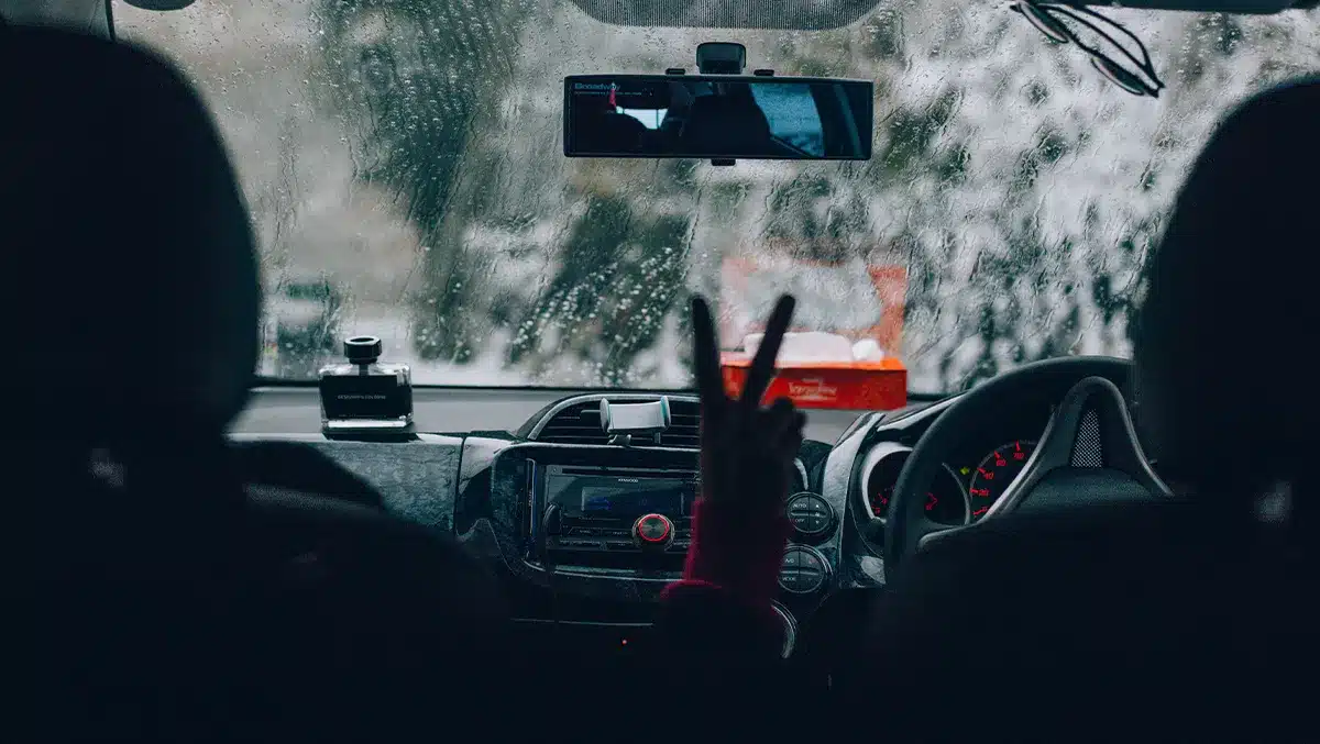 Motorista dirigindo sob forte chuva, com o para-brisa coberto por gotas e baixa visibilidade à frente, simbolizando a importância da manutenção preventiva para evitar aquaplanagem e falhas elétricas durante temporais.