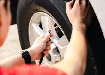 Pessoa calibrando o pneu de um carro com medidor de pressão, representando o cuidado com a manutenção preventiva e a importância de manter a pressão correta para segurança, economia de combustível e durabilidade dos pneus.