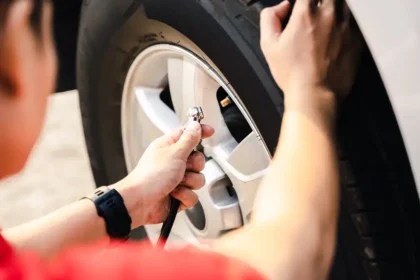 Pessoa calibrando o pneu de um carro com medidor de press&atilde;o, representando o cuidado com a manuten&ccedil;&atilde;o preventiva e a import&acirc;ncia de manter a press&atilde;o correta para seguran&ccedil;a, economia de combust&iacute;vel e durabilidade dos pneus.