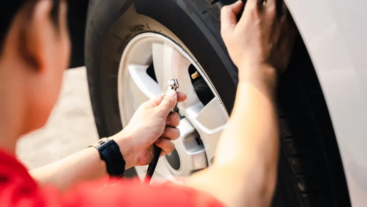 Pessoa calibrando o pneu de um carro com medidor de pressão, representando o cuidado com a manutenção preventiva e a importância de manter a pressão correta para segurança, economia de combustível e durabilidade dos pneus.