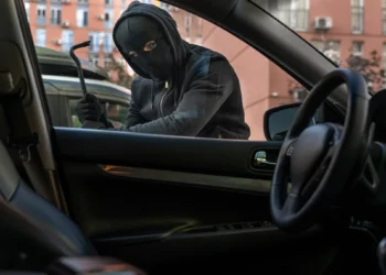 Homem mascarado tentando arrombar a porta de um carro estacionado em área urbana, representando o aumento dos furtos de veículos no Brasil em 2025.