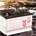 Bateria automotiva sobre o compartimento do motor com símbolo de reciclagem, representando o tema de baterias recondicionadas e novas para veículos.