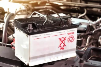 Bateria automotiva sobre o compartimento do motor com símbolo de reciclagem, representando o tema de baterias recondicionadas e novas para veículos.
