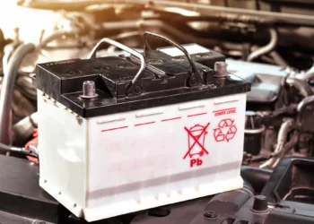Bateria automotiva sobre o compartimento do motor com símbolo de reciclagem, representando o tema de baterias recondicionadas e novas para veículos.