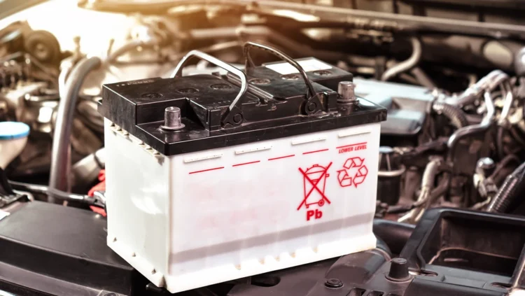Bateria automotiva sobre o compartimento do motor com símbolo de reciclagem, representando o tema de baterias recondicionadas e novas para veículos.