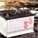 Bateria automotiva sobre o compartimento do motor com símbolo de reciclagem, representando o tema de baterias recondicionadas e novas para veículos.