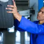 Mecânico realizando o rodízio de pneus em uma oficina, levantando o veículo com macaco hidráulico e verificando o desgaste dos pneus para garantir uma troca equilibrada.