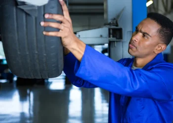 Mecânico realizando o rodízio de pneus em uma oficina, levantando o veículo com macaco hidráulico e verificando o desgaste dos pneus para garantir uma troca equilibrada.