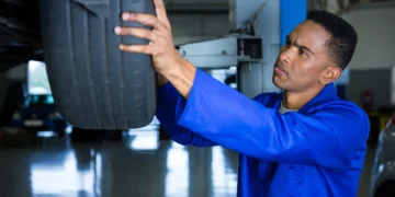 Mecânico realizando o rodízio de pneus em uma oficina, levantando o veículo com macaco hidráulico e verificando o desgaste dos pneus para garantir uma troca equilibrada.