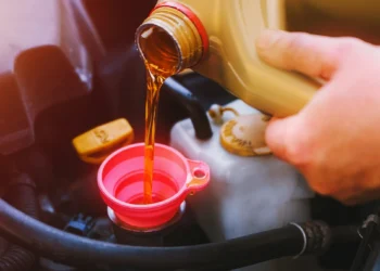 Mão de motorista despejando óleo de motor através de funil rosa em compartimento do carro durante a troca de óleo automotivo, representando manutenção preventiva e cuidados com o veículo.