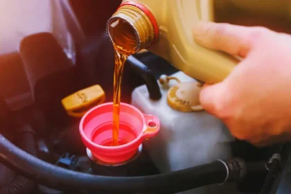 M&atilde;o de motorista despejando &oacute;leo de motor atrav&eacute;s de funil rosa em compartimento do carro durante a troca de &oacute;leo automotivo, representando manuten&ccedil;&atilde;o preventiva e cuidados com o ve&iacute;culo.