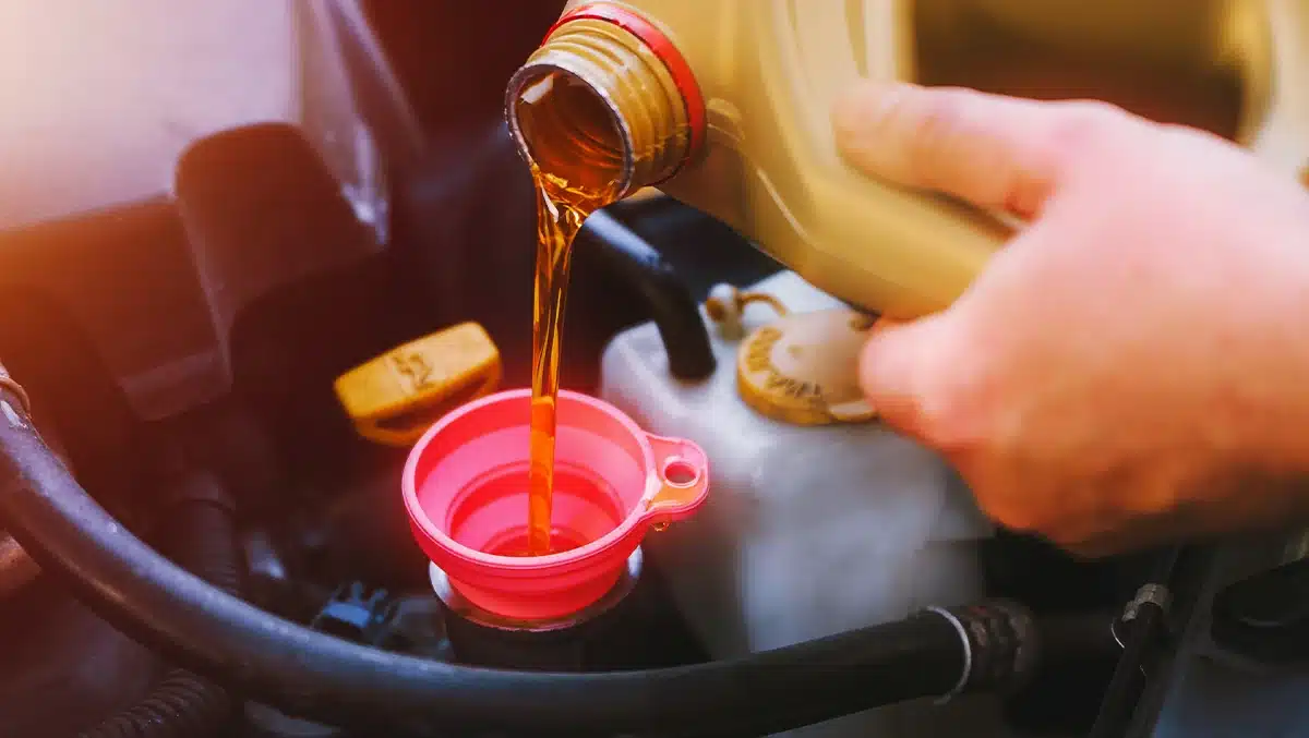 Mão de motorista despejando óleo de motor através de funil rosa em compartimento do carro durante a troca de óleo automotivo, representando manutenção preventiva e cuidados com o veículo.