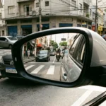 Retrato hiper-realista de retrovisor lateral de carro em rua urbana brasileira, destacando novos requisitos do CONTRAN e segurança no trânsito