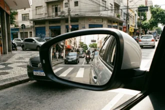 Retrato hiper-realista de retrovisor lateral de carro em rua urbana brasileira, destacando novos requisitos do CONTRAN e segurança no trânsito