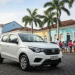 Carro popular estacionado em rua movimentada de Maceió, Alagoas, com prédios e palmeiras ao fundo sob a luz do sol