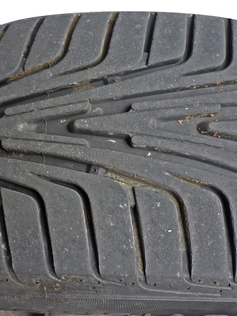 Desgaste do pneu visto de perto: a sigla TWI no ombro aponta a fileira de ressaltos de 1,6 mm no fundo dos sulcos; quando a borracha chega ao nível deles, é hora de trocar.