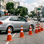 Alterações no trânsito: cones laranjas de trânsito posicionados no asfalto sinalizando interdição em avenida urbana durante o dia.