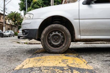 Barulho met&aacute;lico na suspens&atilde;o: roda dianteira de ve&iacute;culo passando por lombada em rua urbana de asfalto, mostrando a compress&atilde;o da suspens&atilde;o ao transpor a ondula&ccedil;&atilde;o.
