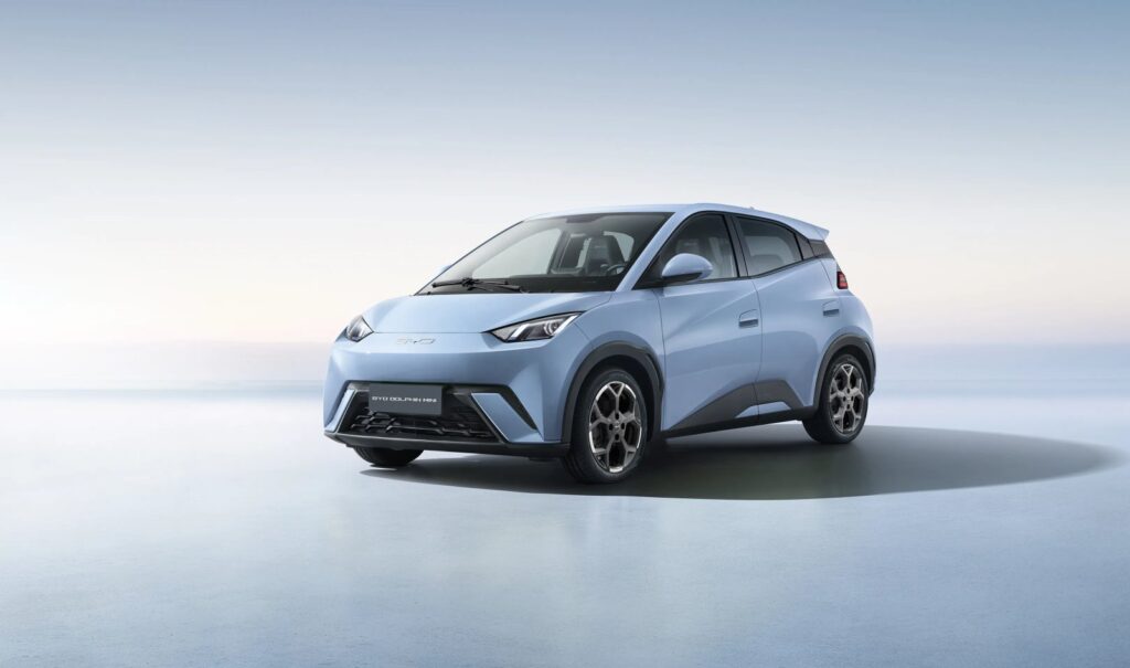 BYD Dolphin Mini tem menor consumo energético no Ranking Mauá com 342 km urbanos 2 BYD Dolphin Mini: carro compacto elétrico conectado a cabo de carregamento em rua arborizada com prédios urbanos ao fundo. — foto 1