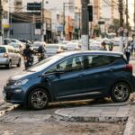 BYD Dolphin Mini: hatch compacto elétrico moderno conectado a ponto de recarga na rua de uma grande cidade brasileira durante o entardecer.