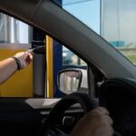 Motorista pagando na cabine de uma praça de pedágio em rodovia, cena para calcular pedágio e combustível da viagem