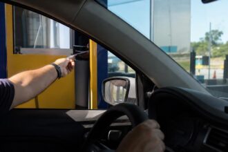 Motorista pagando na cabine de uma praça de pedágio em rodovia, cena para calcular pedágio e combustível da viagem