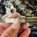 Mecânico segurando uma vela de ignição com o motor ao fundo