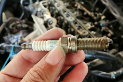 Mecânico segurando uma vela de ignição com o motor ao fundo