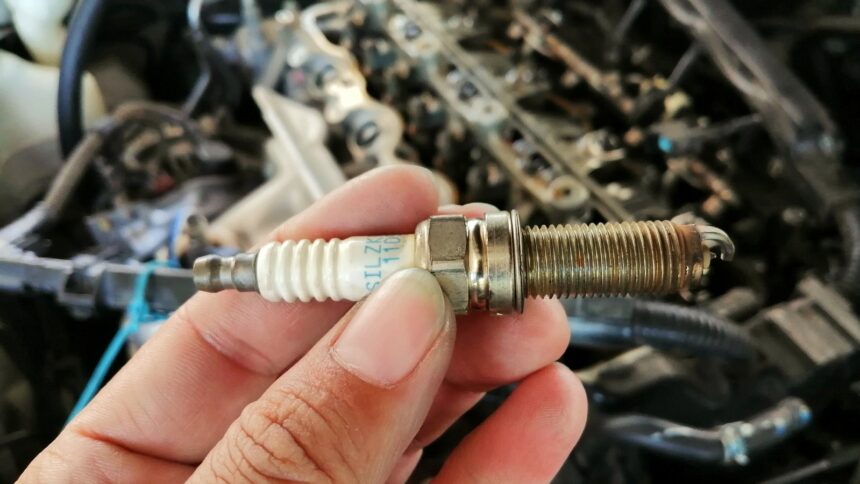 Ponto de ignição: sintomas e como ajustar 1 Mecânico segurando uma vela de ignição com o motor ao fundo