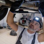 Mecânico com lanterna inspecionando a caixa de direção por baixo do carro