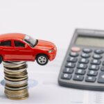 Carrinho sobre pilha de moedas e calculadora, simulação do IPVA 2027