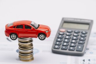 Carrinho sobre pilha de moedas e calculadora, simulação do IPVA 2027