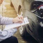 Pessoa anotando os danos de um carro batido, tema de proteção veicular e seguro