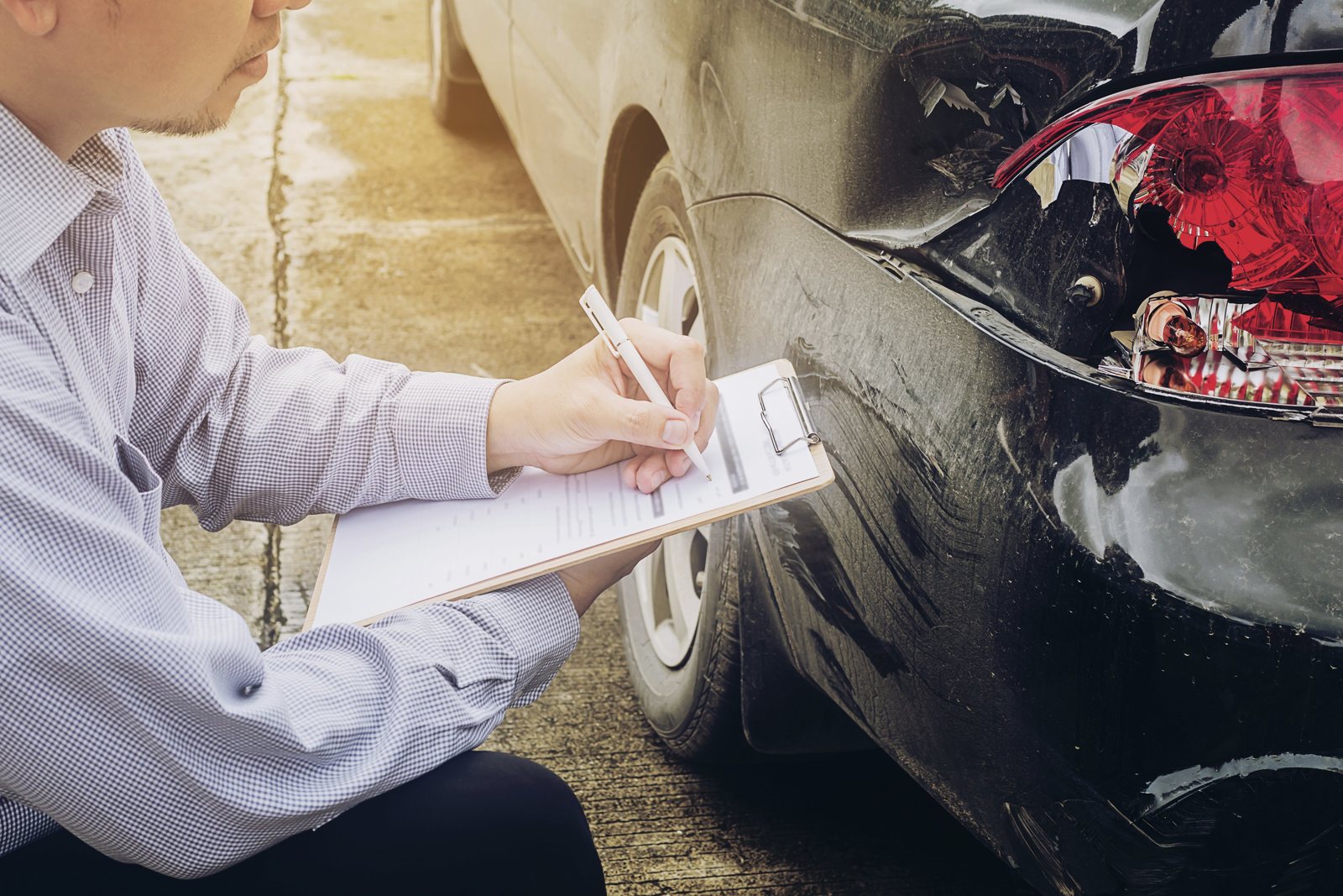 Pessoa anotando os danos de um carro batido, tema de proteção veicular e seguro