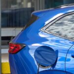 Carro elétrico novo ou usado a combustão: conector de estação de recarga plugado em veículo elétrico urbano moderno.