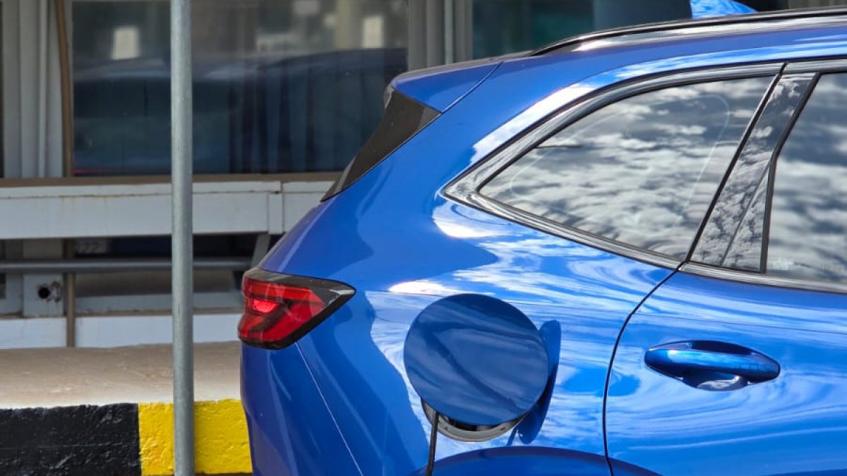 Carro elétrico novo ou usado a combustão: conector de estação de recarga plugado em veículo elétrico urbano moderno.