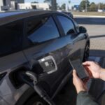Como achar pontos de recarga de carro elétrico: motorista consulta no celular o mapa de pontos de recarga ao lado de um carro elétrico plugado