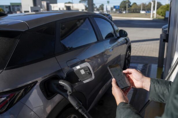 Como achar pontos de recarga de carro elétrico: motorista consulta no celular o mapa de pontos de recarga ao lado de um carro elétrico plugado