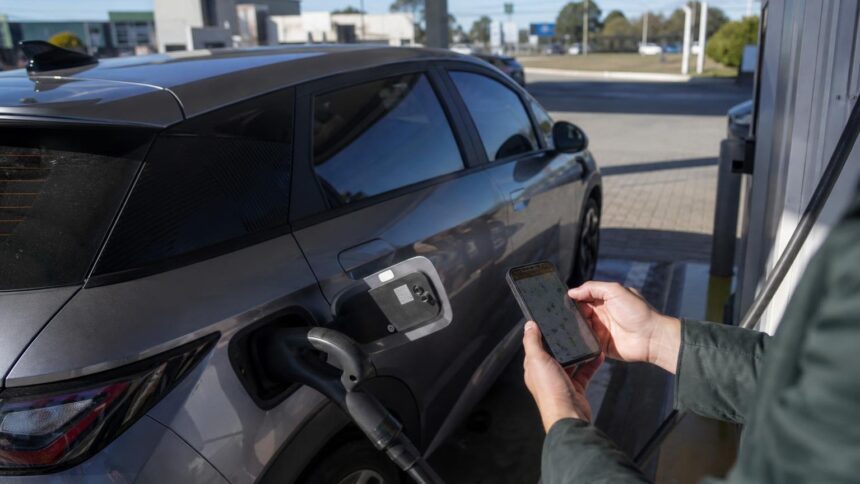 Como achar pontos de recarga de carro elétrico no mapa: Google Maps, apps das redes e o conector certo 1 Como achar pontos de recarga de carro elétrico: motorista consulta no celular o mapa de pontos de recarga ao lado de um carro elétrico plugado