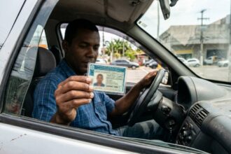 Motorista segura a CNH aberta dentro do veículo mostrando atenção a pendências de CPF irregular na CNH.