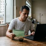 Motorista faz a Detran PR consulta Renavam do IPVA no notebook, com o documento do carro