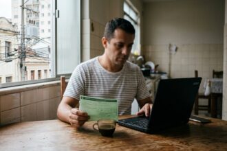 Motorista faz a Detran PR consulta Renavam do IPVA no notebook, com o documento do carro