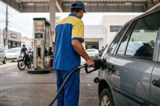 Gasolina em alta floresta: bico injetor de combustível inserido no bocal do tanque de um carro popular durante abastecimento em posto brasileiro.
