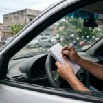 IPVA 2027 estimado no RJ: motorista fazendo cálculos financeiros com bloco de notas apoiado no volante dentro do veículo.