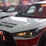 Licenciamento 2026 sp: mãos de motorista segurando celular no interior de um carro brasileiro, com volante e chave ao lado em foco.