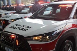 Licenciamento 2026 sp: mãos de motorista segurando celular no interior de um carro brasileiro, com volante e chave ao lado em foco.