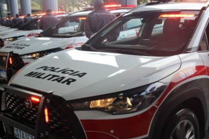 Licenciamento 2026 sp: m&atilde;os de motorista segurando celular no interior de um carro brasileiro, com volante e chave ao lado em foco.