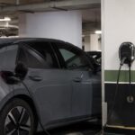 Ponto de recarga de carro elétrico em condomínio: carregador de parede ligado a um carro elétrico na vaga de garagem de um condomínio