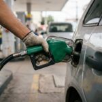 Preço do etanol: mão de frentista segurando bico de combustível inserido no bocal do tanque de um carro popular em posto urbano.